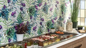 A kitchen with a floral wallpaper, a fruit and cheese board, and a window with plants. - Thon Hotel Storgata (Kristiansund)