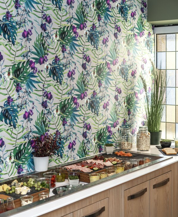 A kitchen with a floral wallpaper, a fruit and cheese board, and a window with plants. - Thon Hotel Storgata (Kristiansund)