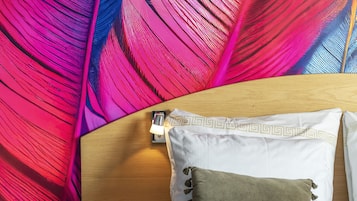 Una cama con ropa blanca y almohada marrón, cabecero de madera y pared con diseño de plumas de colores.
