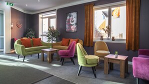A modern lobby with a green sofa, a pink chair, and a yellow armchair. There is a wooden table and a potted plant. - Thon Hotel Storgata (Kristiansund)