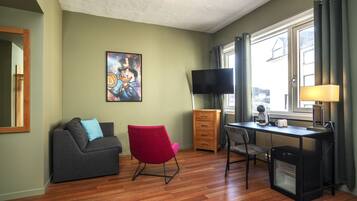 A modern living room with a grey sofa, a red chair, a wooden desk, and a television.