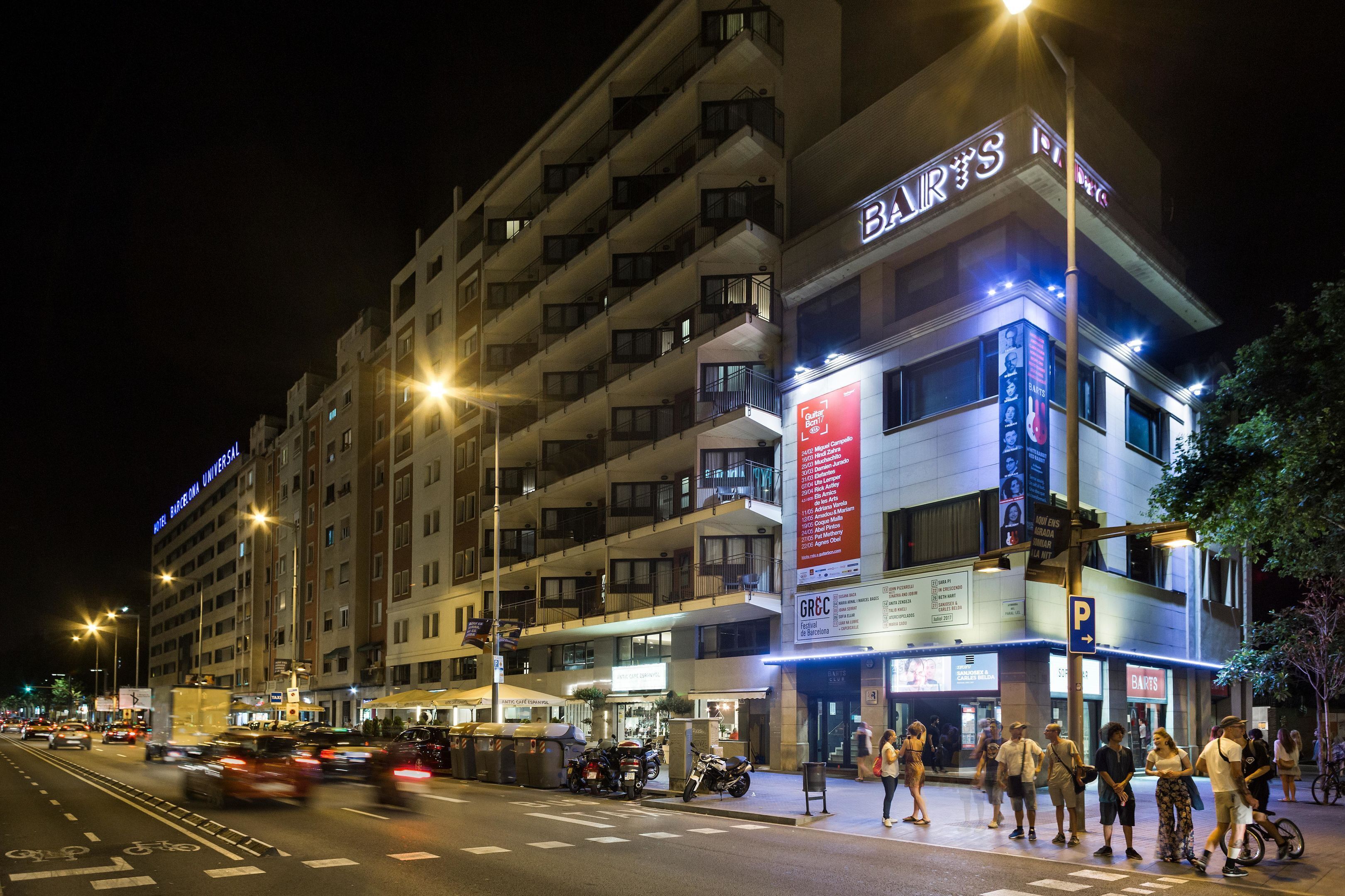 Un hotel de varios pisos con balcones, un bar a la vista y un cartel de estacionamiento.
