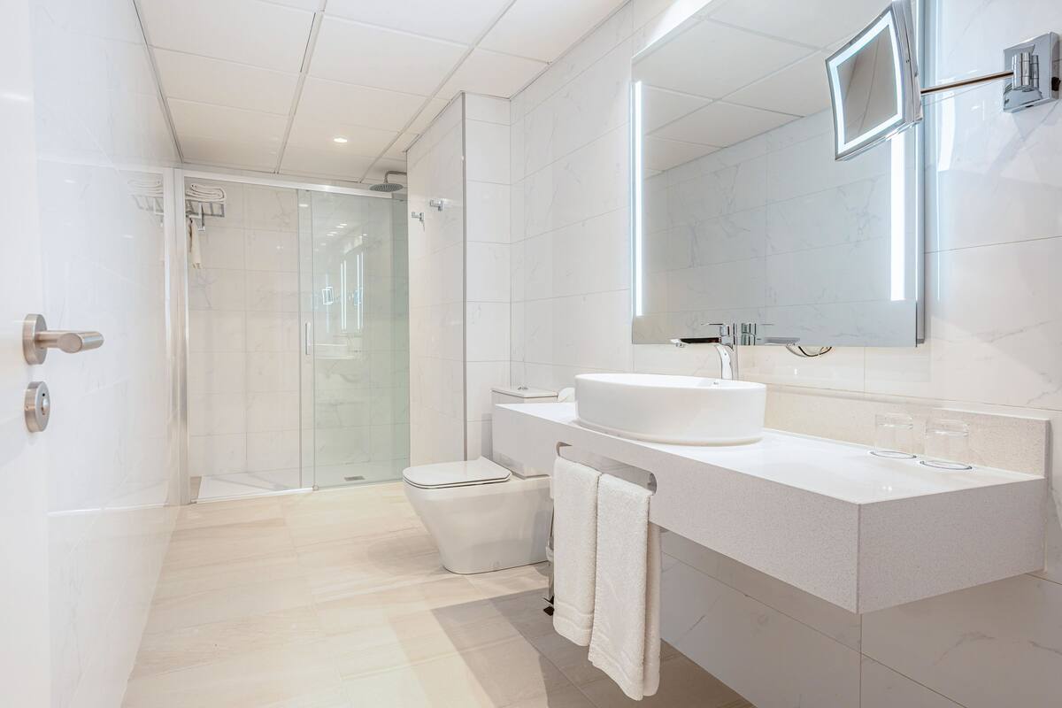 Un baño moderno con ducha de vidrio, lavamanos blanco y un espejo grande.