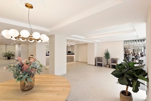 Un vestíbulo espacioso con una mesa redonda de madera, una planta grande en maceta y un candelabro moderno.