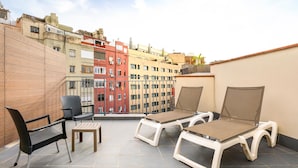 A rooftop terrace with two sun loungers, a small table, and a chair. The terrace has a tiled floor and overlooks a row of colorful buildings. - Hotel Best Auto Hogar (Barcelona)