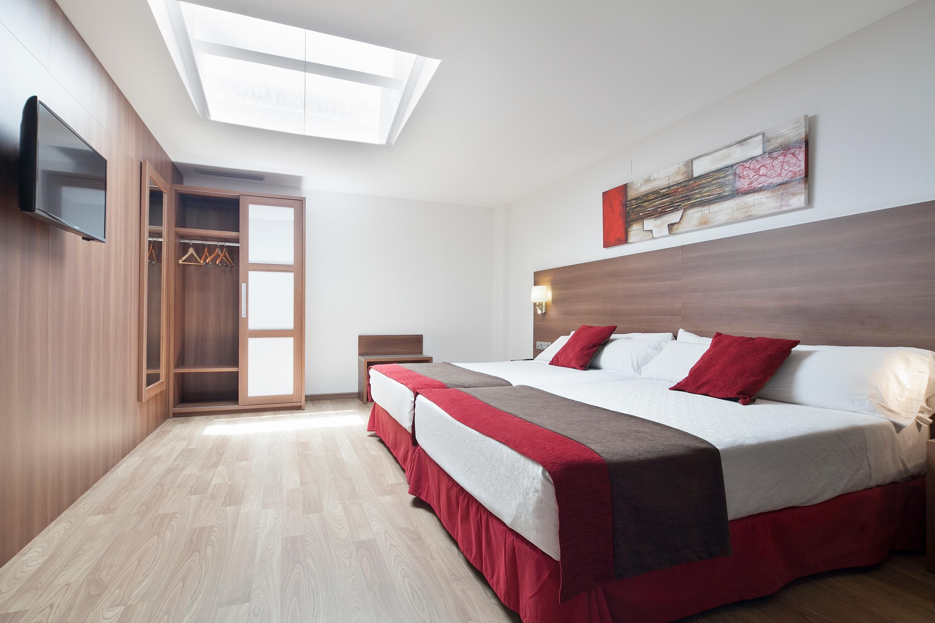 A modern hotel room with a large bed, a walk-in closet, a flat-screen TV, and a skylight.