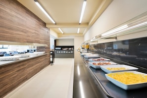 Un espace buffet comprenant plusieurs stands de nourriture et un comptoir avec des places assises.