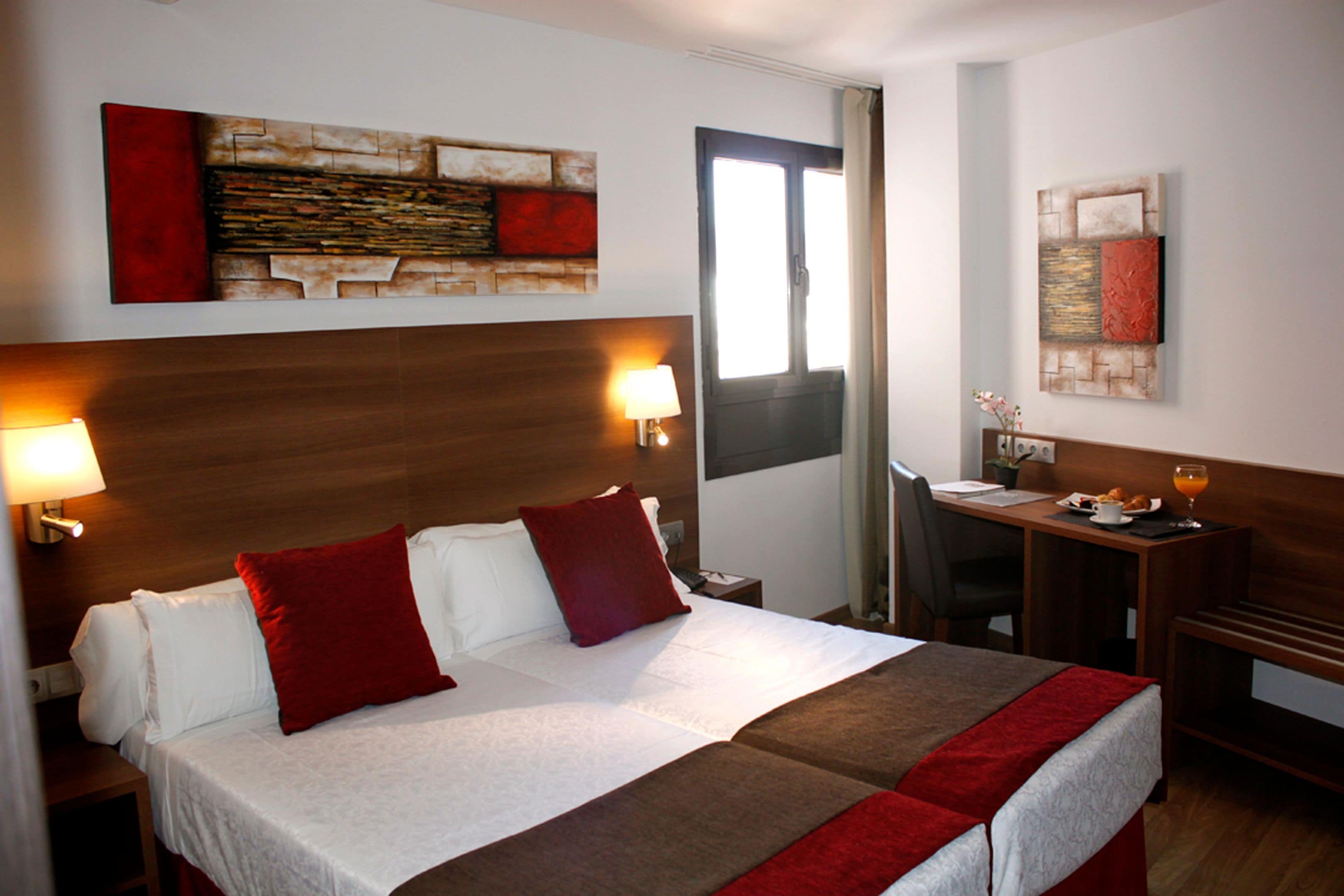 Una habitación de hotel con una cama grande, dos lámparas de noche, un escritorio con silla y obras de arte en las paredes.