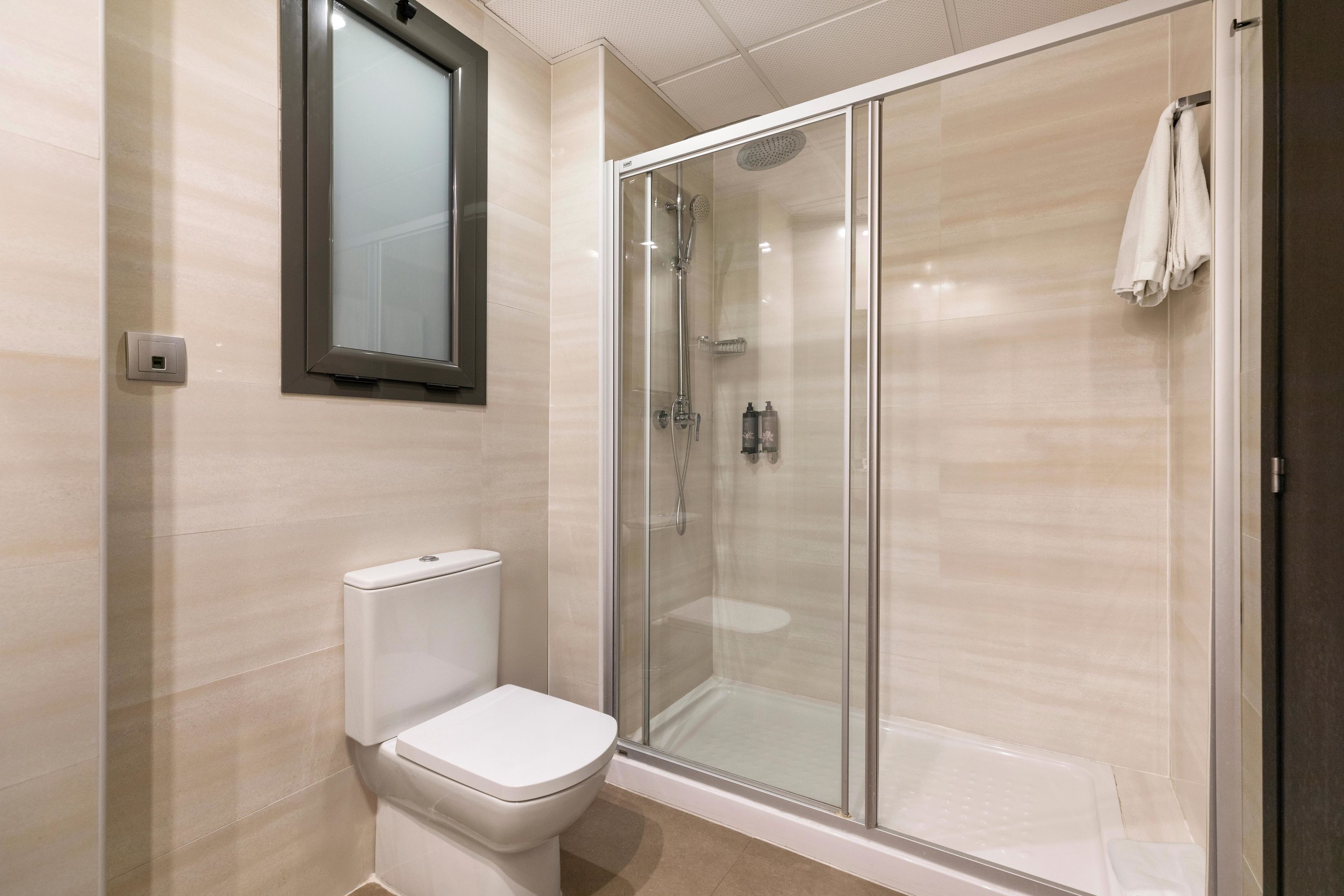 Un baño moderno con inodoro, ducha con mampara de vidrio y una toalla colgada en la pared.