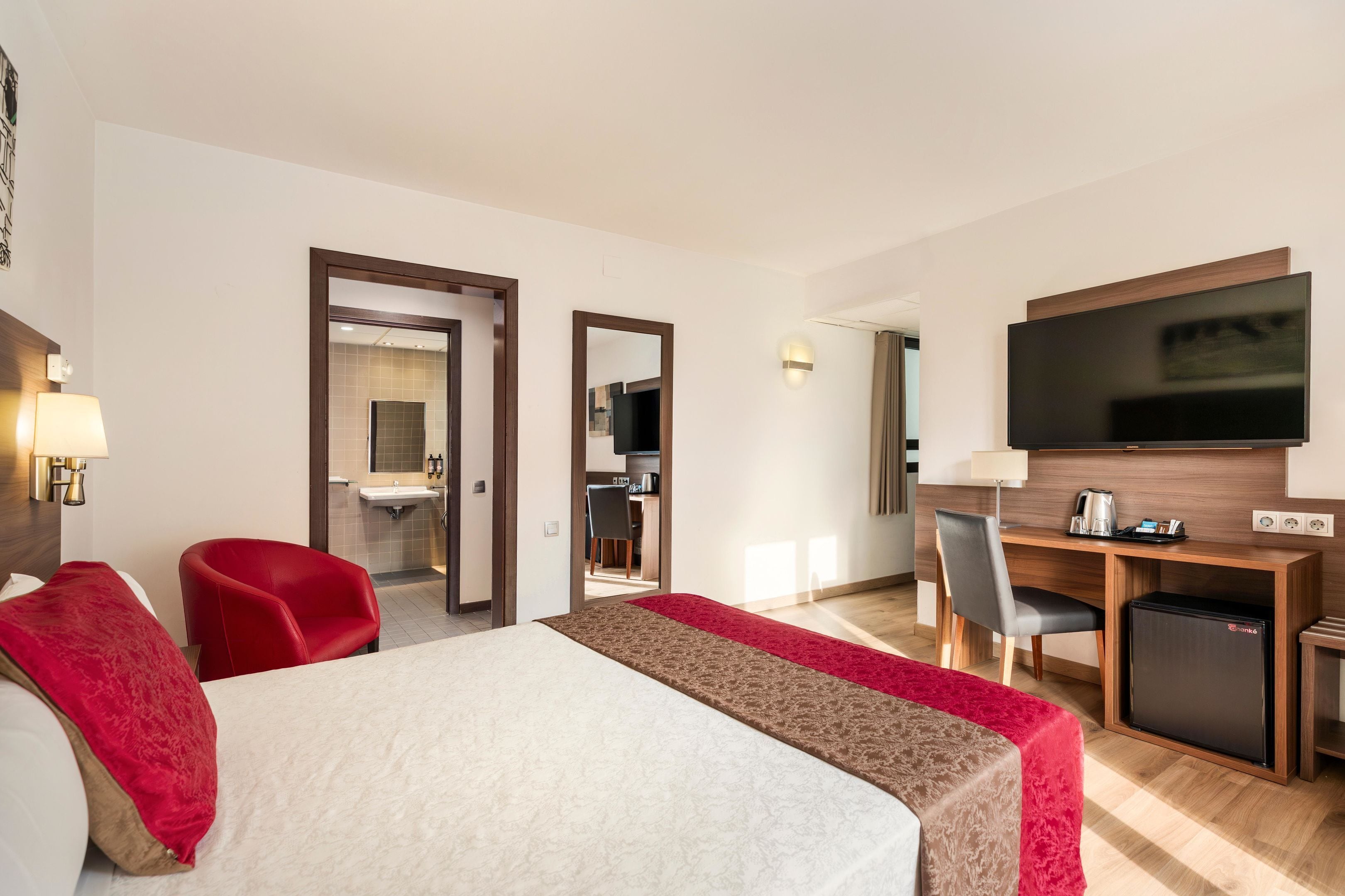 A hotel room with a bed, a desk, a TV, and a small fridge.