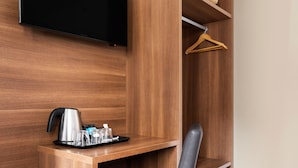 A hotel room with a wooden desk, a black chair, a flat-screen TV mounted on the wall, and a wooden hanger on a shelf. - Hotel Best Auto Hogar (Barcelona)
