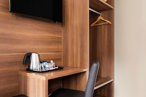 Habitación de hotel con un escritorio de madera, una silla negra, un televisor de pantalla plana montado en la pared y un perchero de madera en un estante.