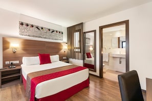 A hotel room with a large bed, a wooden headboard, a red throw blanket, a nightstand with a lamp, a mirror, and a bathroom visible through an open door. - Hotel Best Auto Hogar (Barcelona)