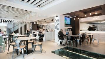 Un restaurante moderno con diversas opciones de asientos, como mesas redondas y sillas, y una cocina a la vista.
