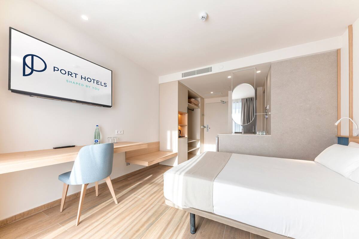 Una habitación de hotel moderna con cama, escritorio, silla, espejo y armario.