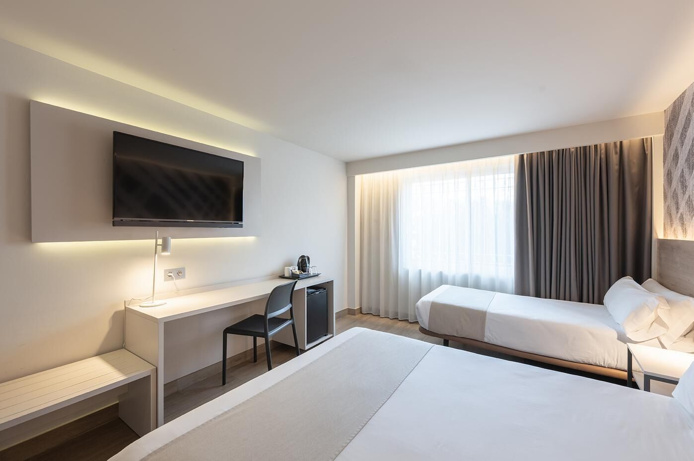 Habitación de hotel con una cama grande, un escritorio con silla, un televisor de pantalla plana y una ventana con cortinas.