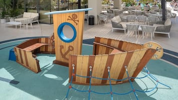 A children's play area with a wooden boat structure, a circular window, and a rope net.