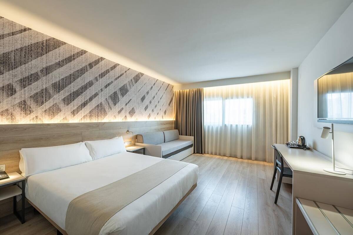 Habitación de hotel moderna con una cama grande, un escritorio, un sofá y un televisor.