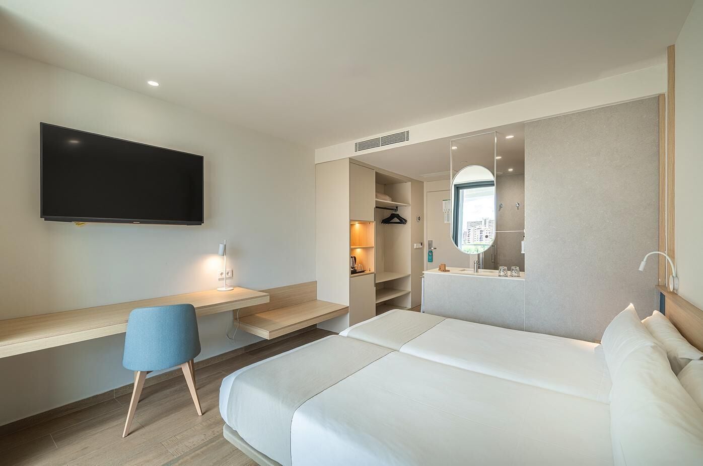 Ett modernt hotellrum med en stor säng, ett skrivbord med en stol, en tv som är monterad på väggen och en rymlig klädkammare.