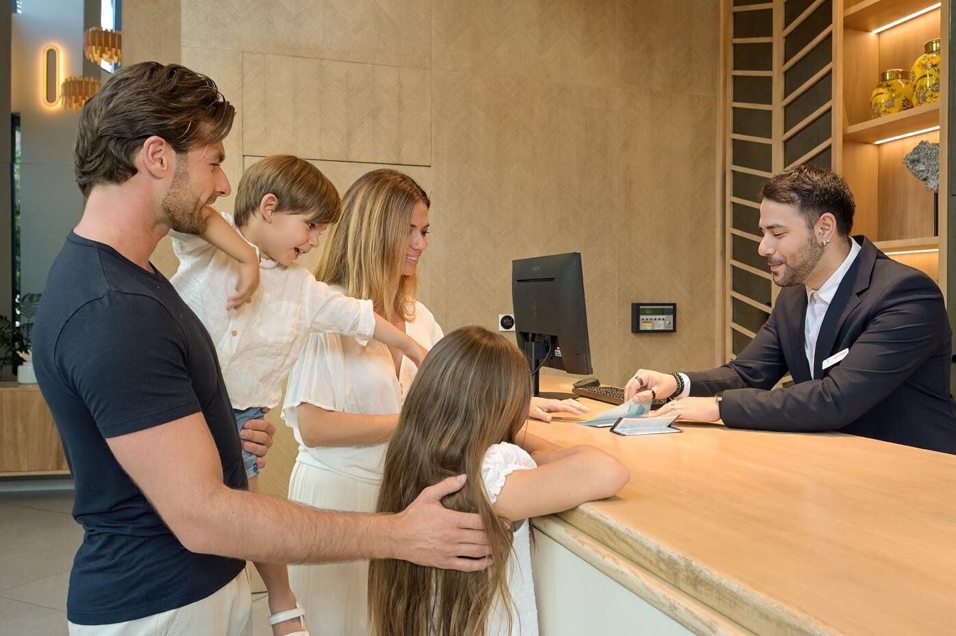 A hotel reception area with a wooden reception desk, a computer monitor, and a digital display.