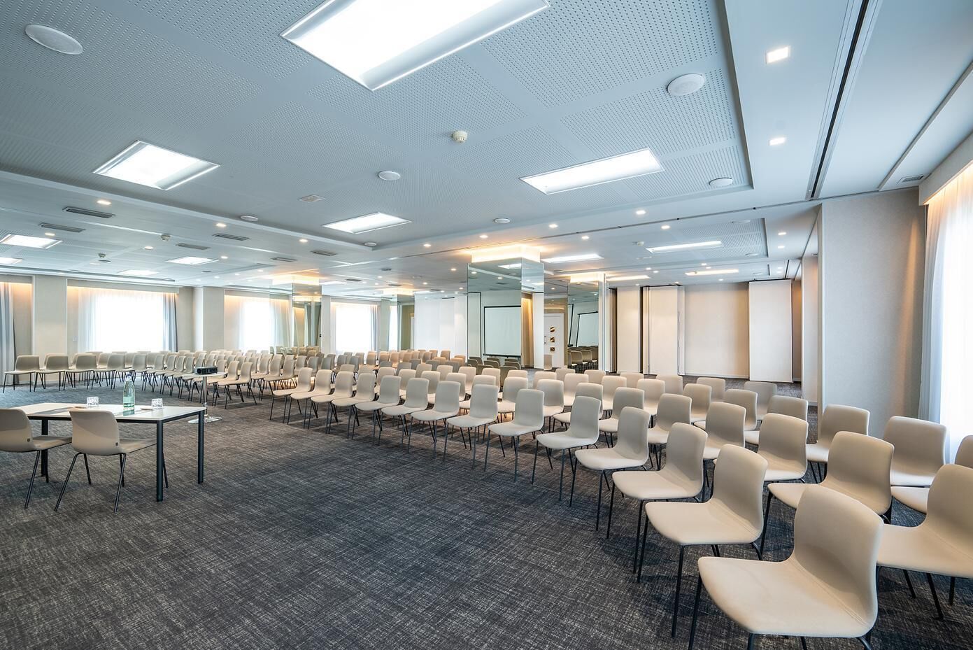 A conference room with rows of chairs, a large table, and a projector screen.