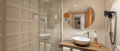 Un baño moderno con ducha de vidrio, tocador de madera con lavamanos grande y espejo redondo.