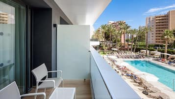 A balcony with white chairs and a table, overlooking a pool with lounge chairs and palm trees.