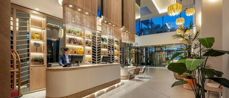A modern hotel lobby with a reception desk, seating area, and large windows.