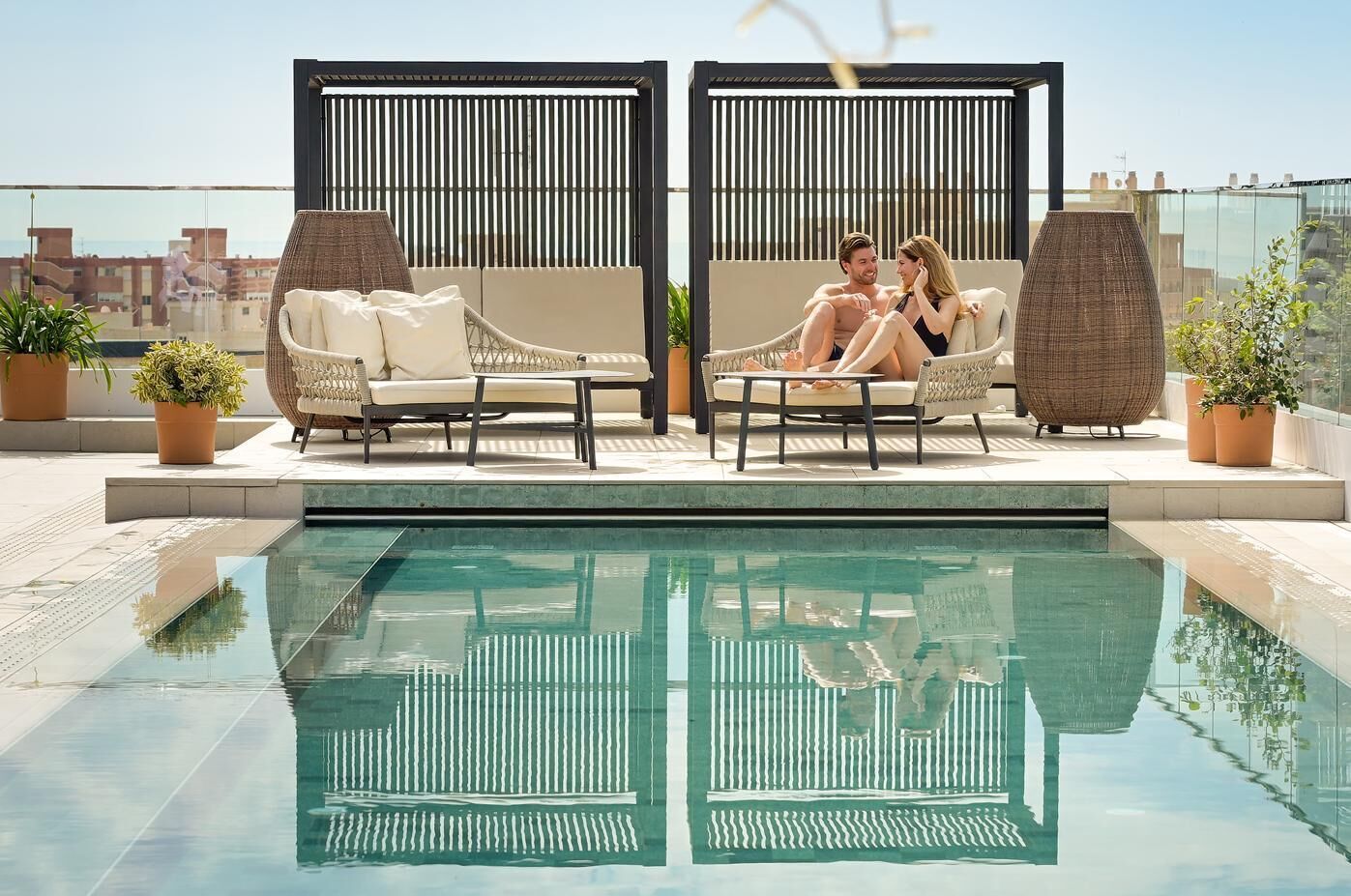 Et tagområde med swimmingpool, to liggestole og et bord, omgivet af plantekasser.