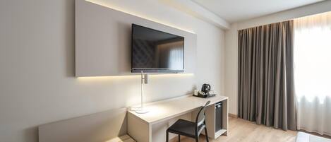 Una habitación de hotel moderna con un televisor de pantalla plana montado en la pared, un escritorio con una silla, un banco y una cafetera.