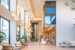 Un hall d’entrée spacieux, agrémenté de lustres modernes, de sièges confortables et de grandes fenêtres offrant une vue sur l’extérieur.