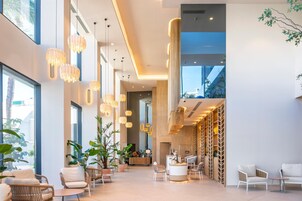 Un hall d’entrée spacieux, agrémenté de lustres modernes, de sièges confortables et de grandes fenêtres offrant une vue sur l’extérieur.