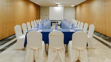 Una sala de conferencias con una mesa larga, sillas blancas y una pantalla para proyector.
