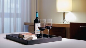 Una bandeja con una botella de vino y dos copas de vino tinto sobre una mesa, junto con un libro y una caja.