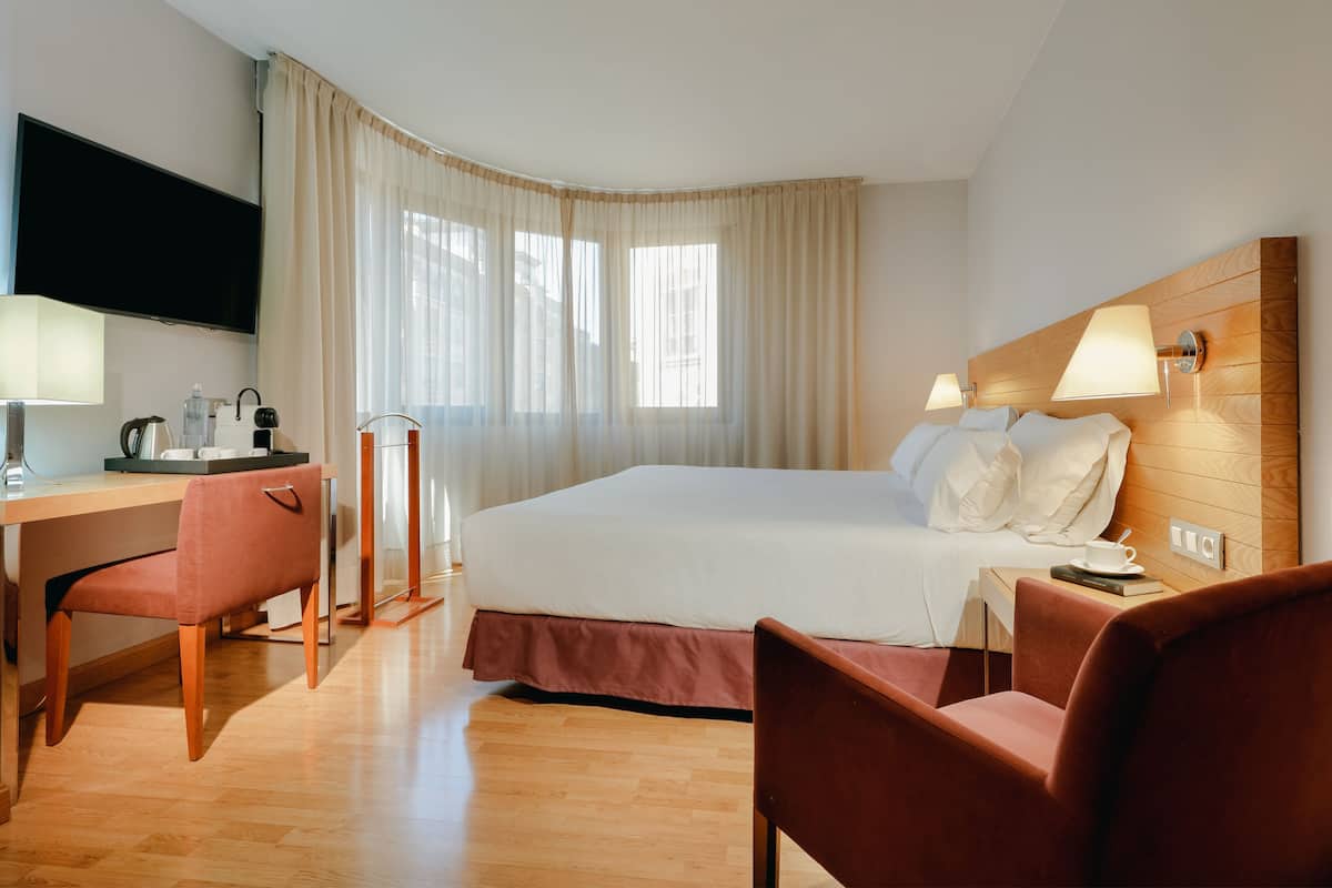 A hotel room with a bed, desk, chairs, and a TV.