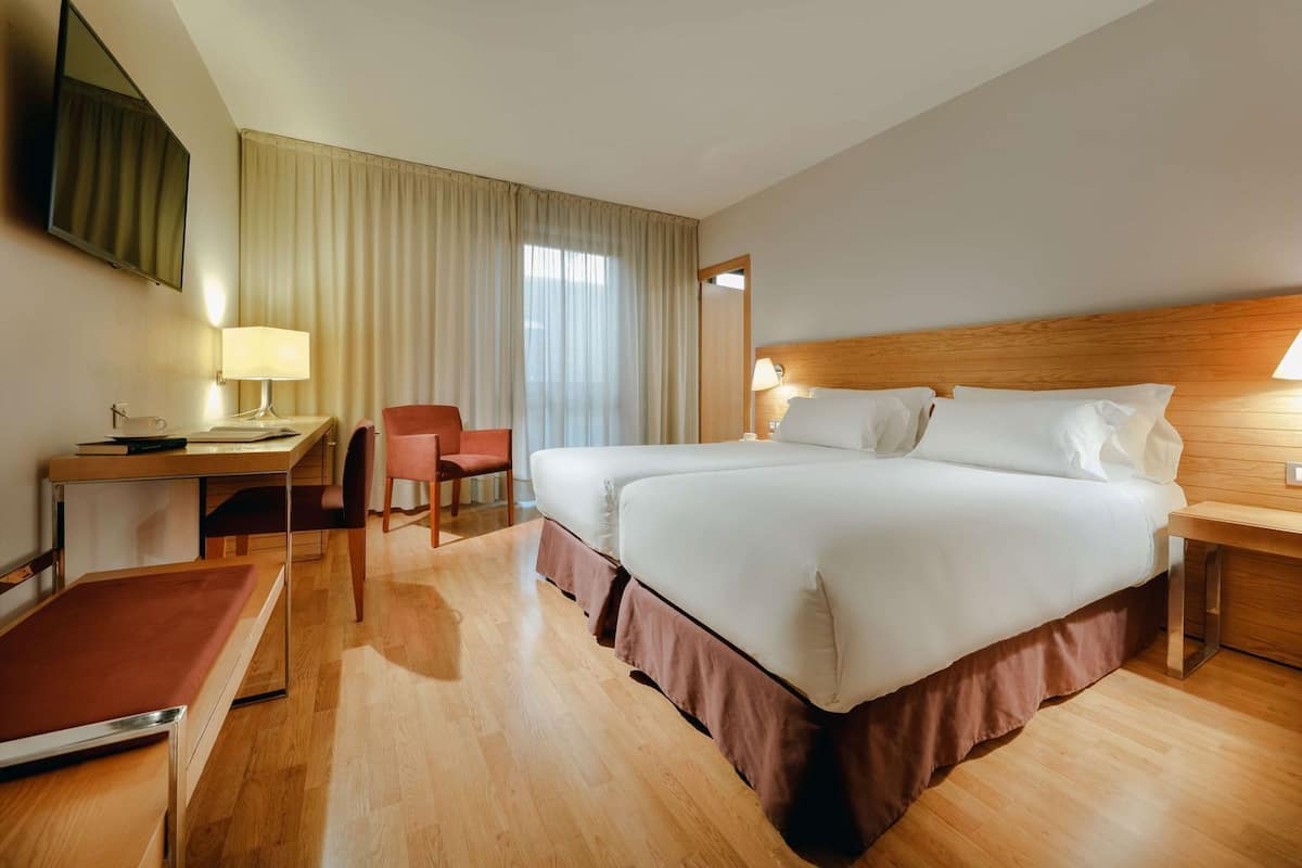 A hotel room with a bed, desk, chair, and a TV.