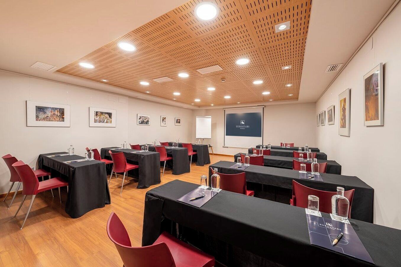 Un salón de conferencias con varias mesas, sillas rojas y techo de madera con iluminación empotrada.
