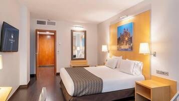 Una habitación de hotel con una cama grande, un cabecero de madera, un televisor de pantalla plana, un espejo y un cuadro de un edificio.
