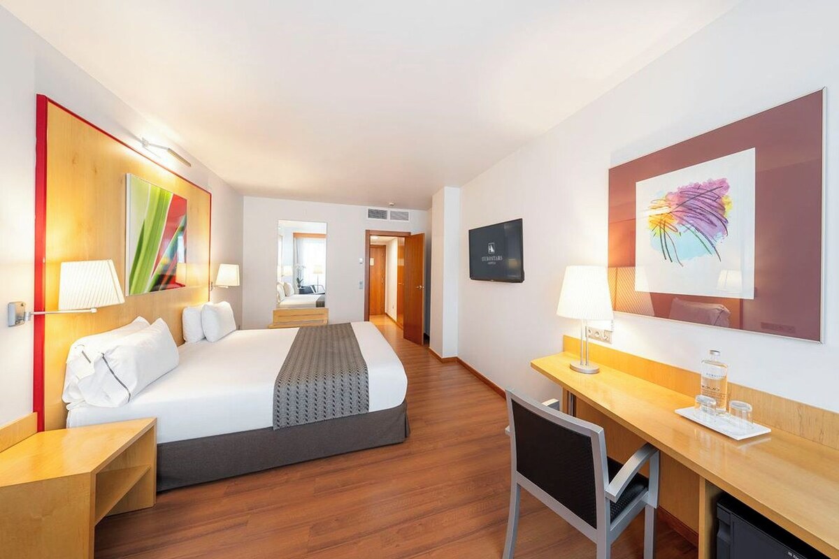 Habitación de hotel con cama, escritorio, silla y obras de arte en las paredes.