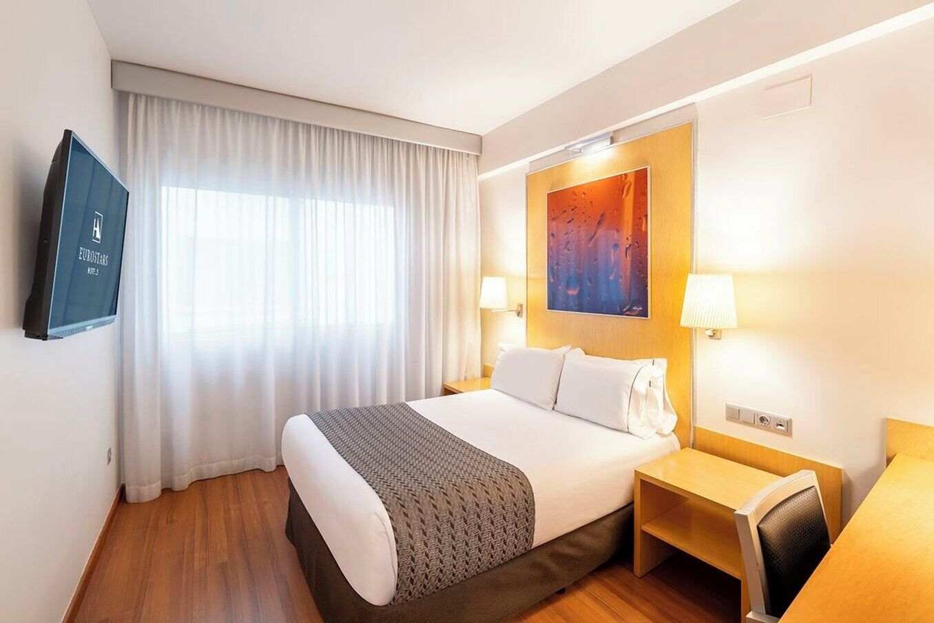 Une chambre d’hôtel avec un grand lit, un bureau, une chaise, une télévision et un tableau au mur.