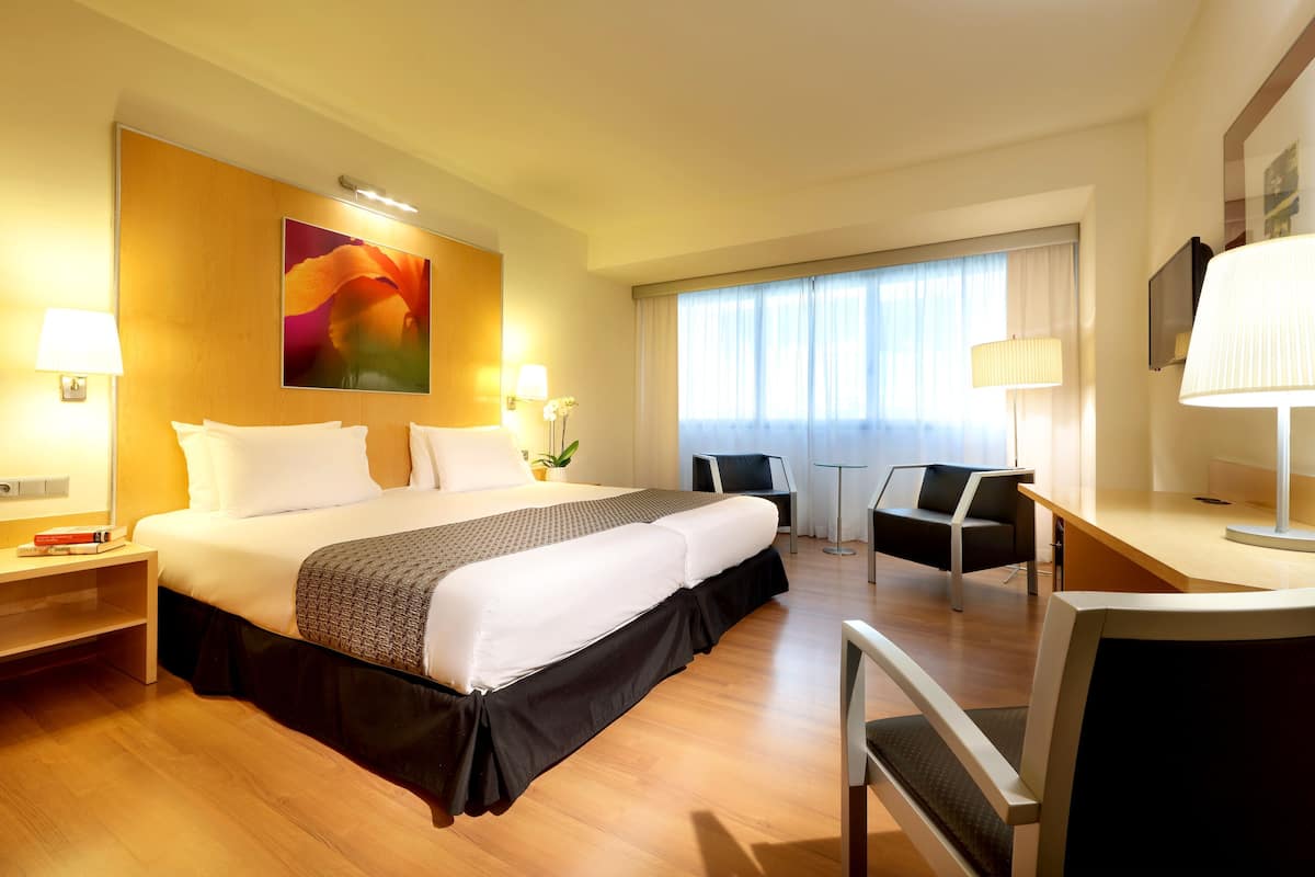 Een hotelkamer met een bed, bureau, stoel, lamp en een groot raam.