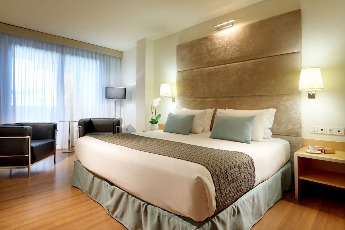 Een hotelkamer met een groot bed, een bureau, een stoel, een televisie en een nachtkastje met een lamp.