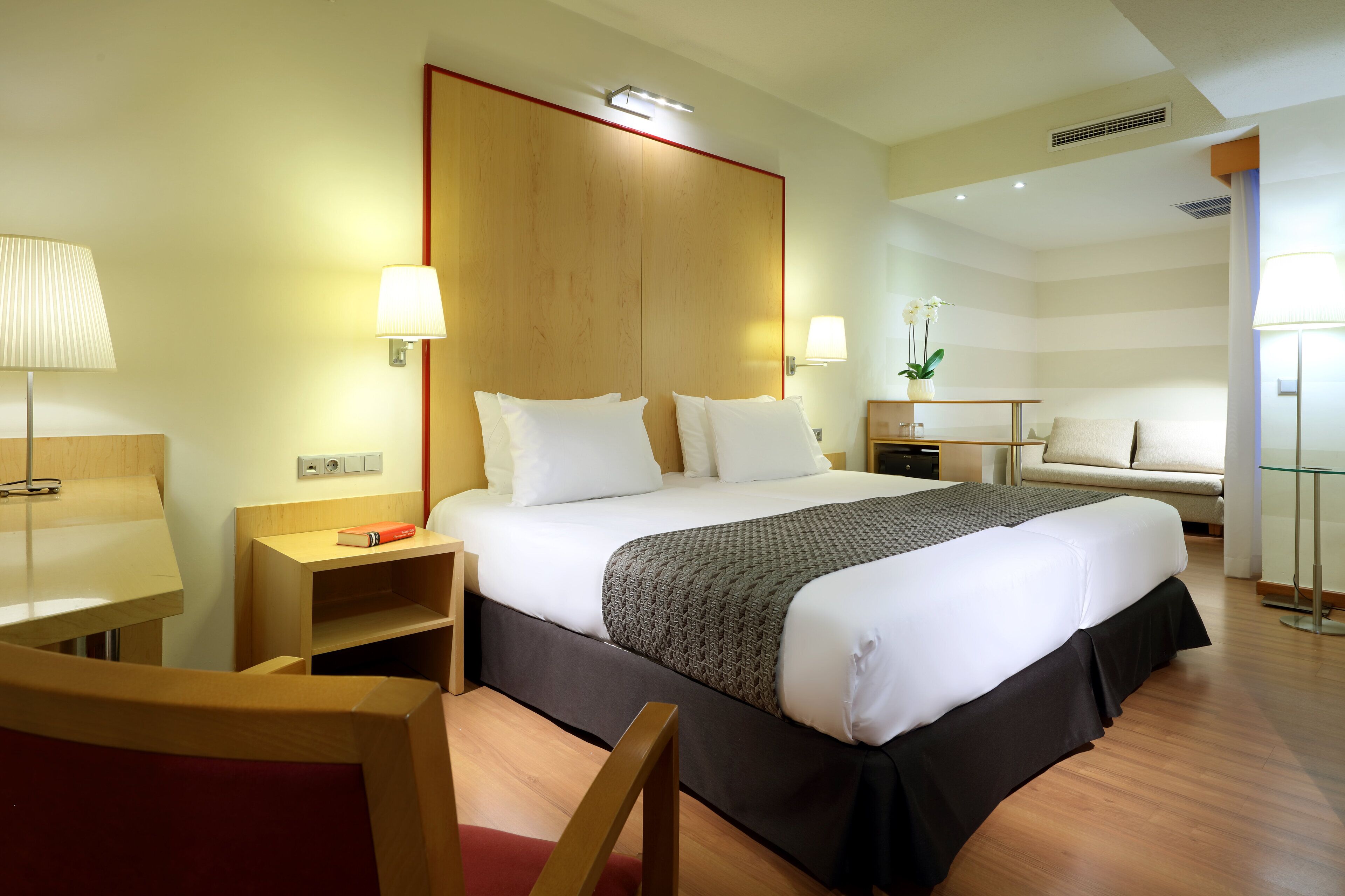 Una habitación de hotel con una cama grande, mesitas de noche, un escritorio y una silla.