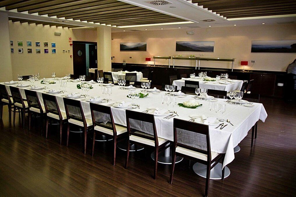 Una larga mesa de comedor preparada para una comida formal, con múltiples sillas, manteles blancos y cristalería.