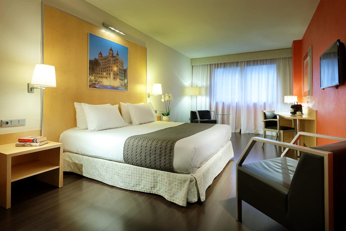 Een hotelkamer met een bed, nachtkastje, lamp, stoel, bureau en een televisie.