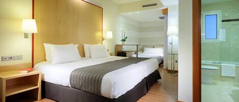 Habitación de hotel con una cama grande, lámparas de noche, una mesita de noche y una pequeña mesa con un jarrón, además de vistas al baño.