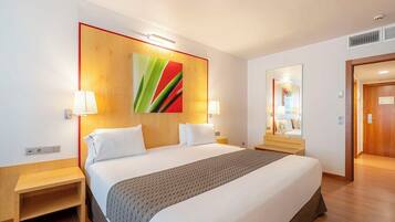 A hotel room with a large bed, two bedside tables, a wooden headboard, a wall-mounted mirror, and a colorful abstract painting.