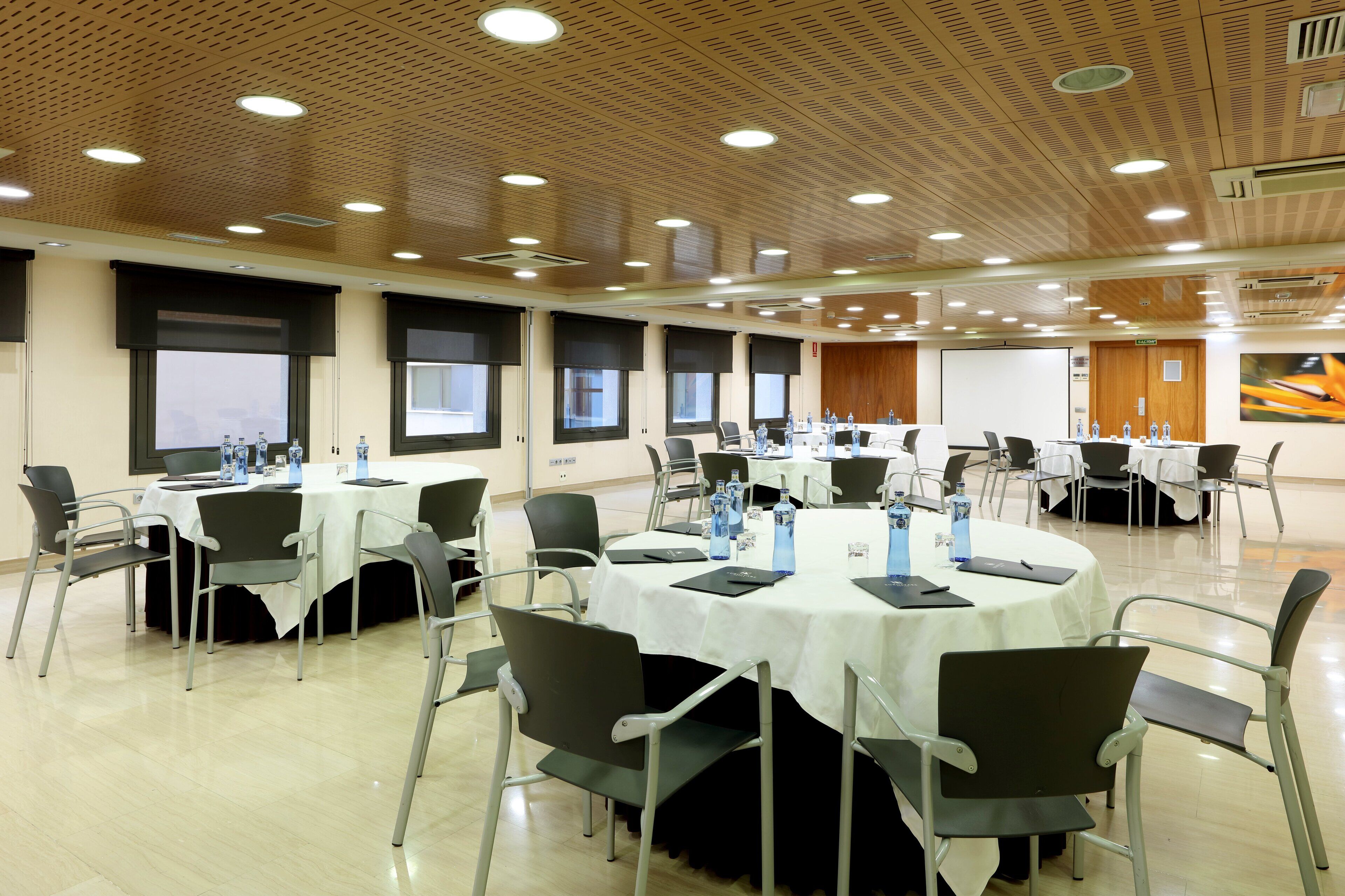 Un salón de conferencias con varias mesas, sillas y pantallas de presentación.