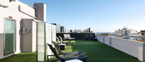 Relax on the rooftop terrace with a clear view of the city skyline, featuring sun loungers and a table for a peaceful retreat.