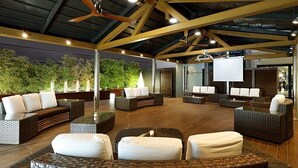 An outdoor lounge area with wicker furniture, a ceiling fan, and a large screen for presentations.